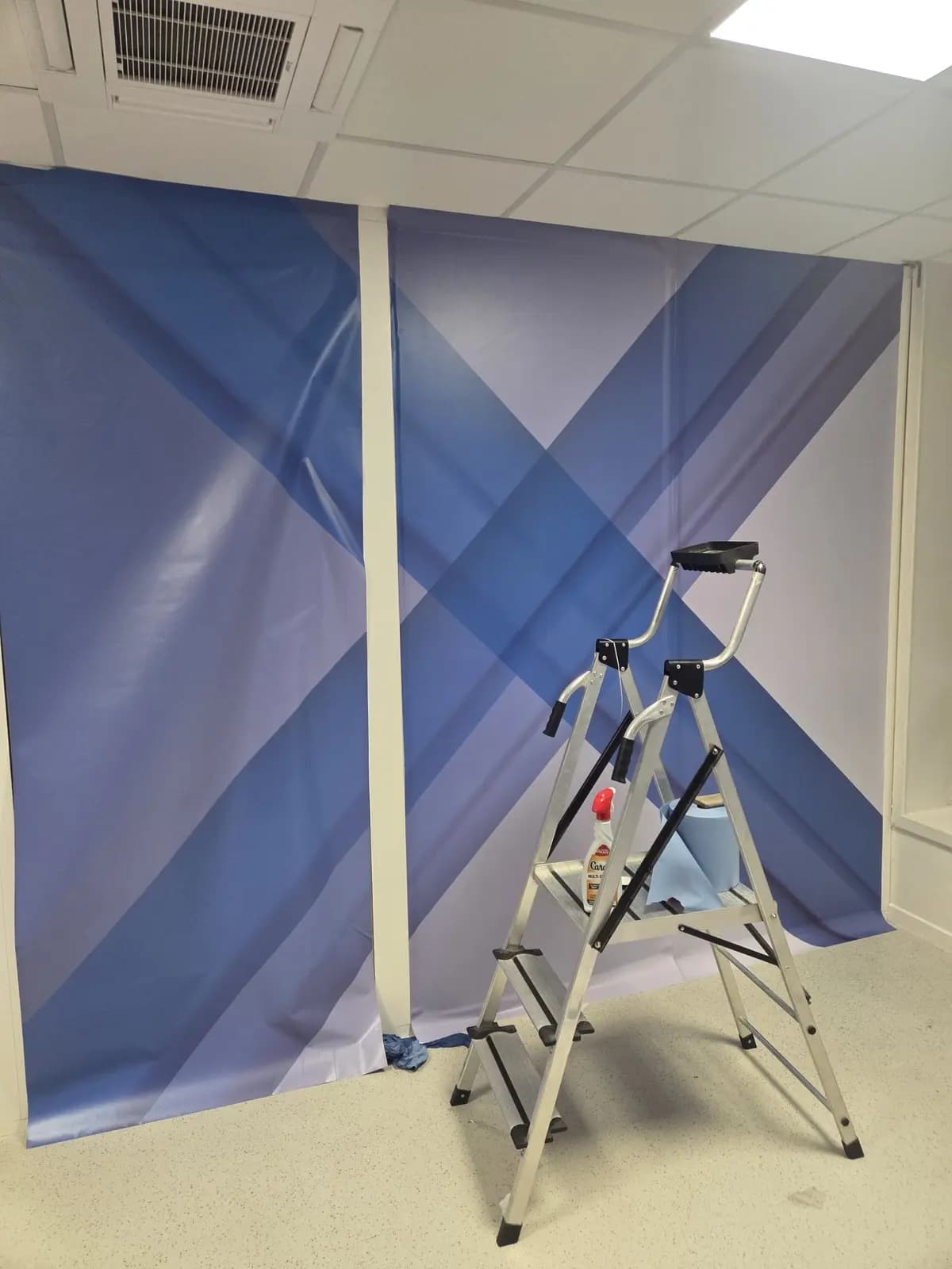 Mur de bureau recouvert d'un adhésif décoratif bleu avec escabeau de pose