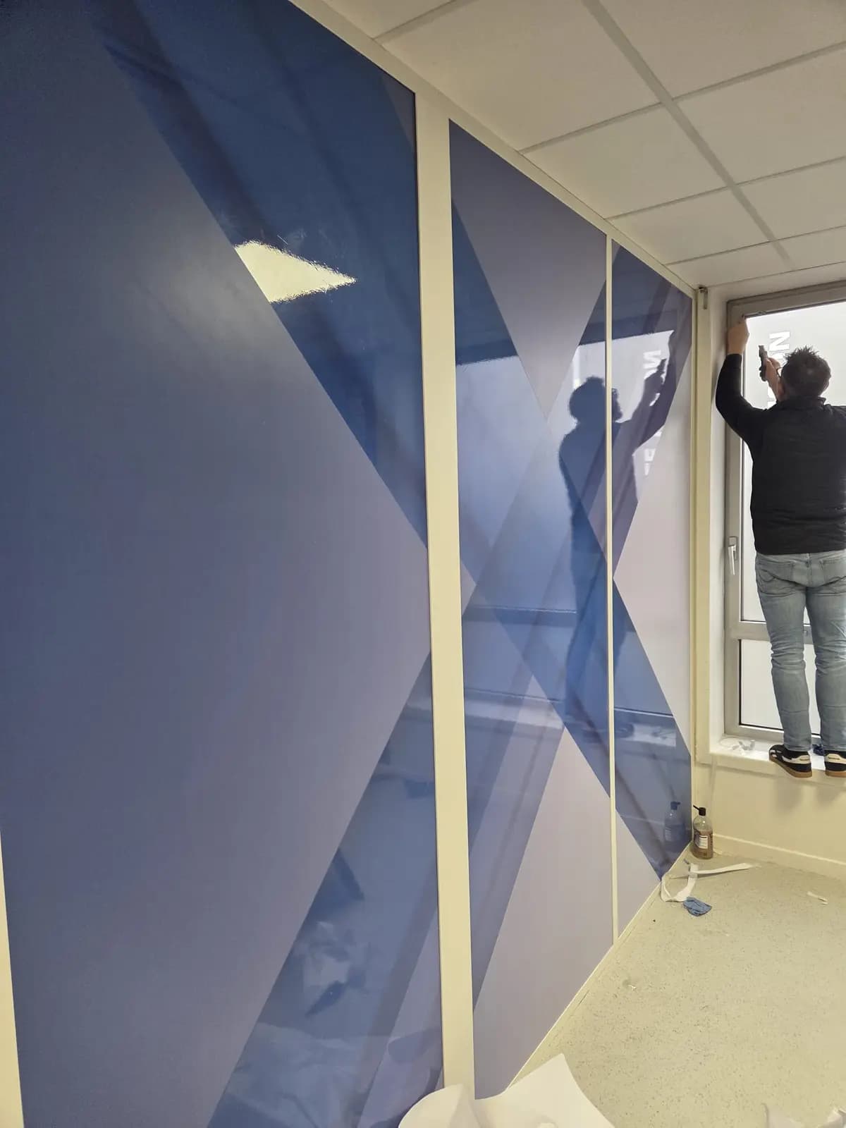 Poseur installant un adhésif mural décoratif près d'une fenêtre de bureau
