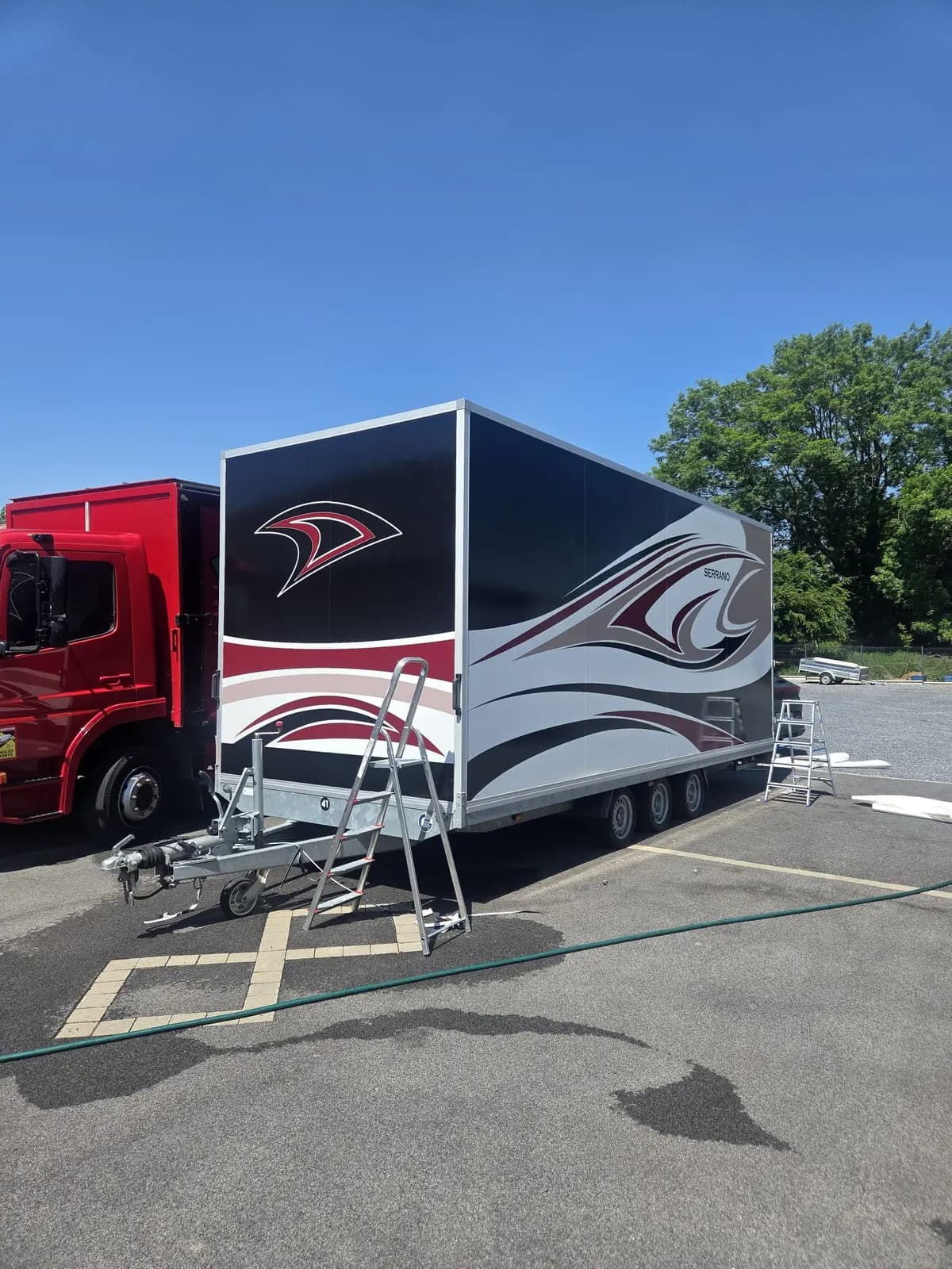 Semi-remorque foraine avec covering décoratif noir rouge et argent derrière un camion rouge