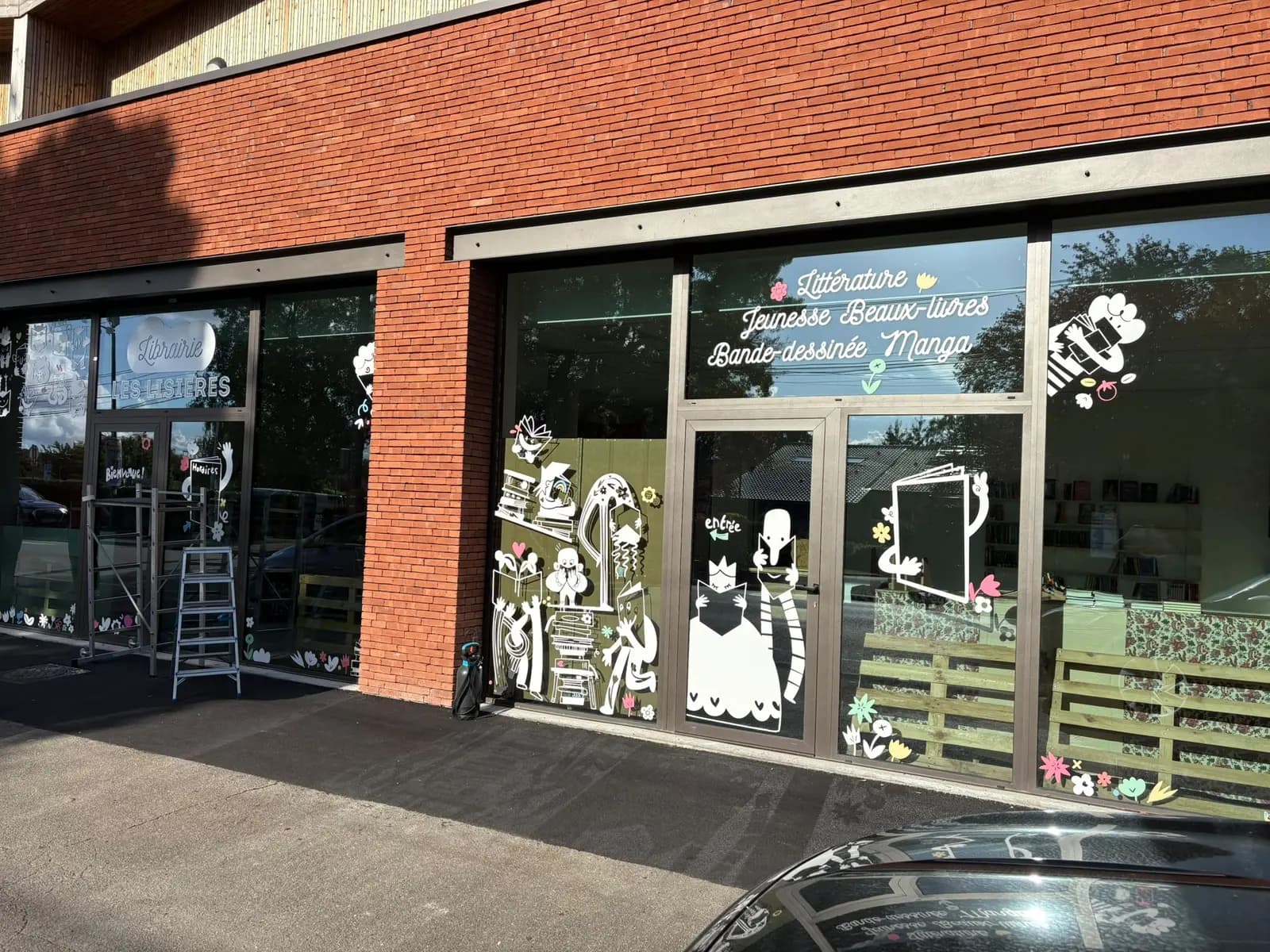 Vitrine de la librairie Les Lisières décorée d'adhésifs découpés blancs illustrés